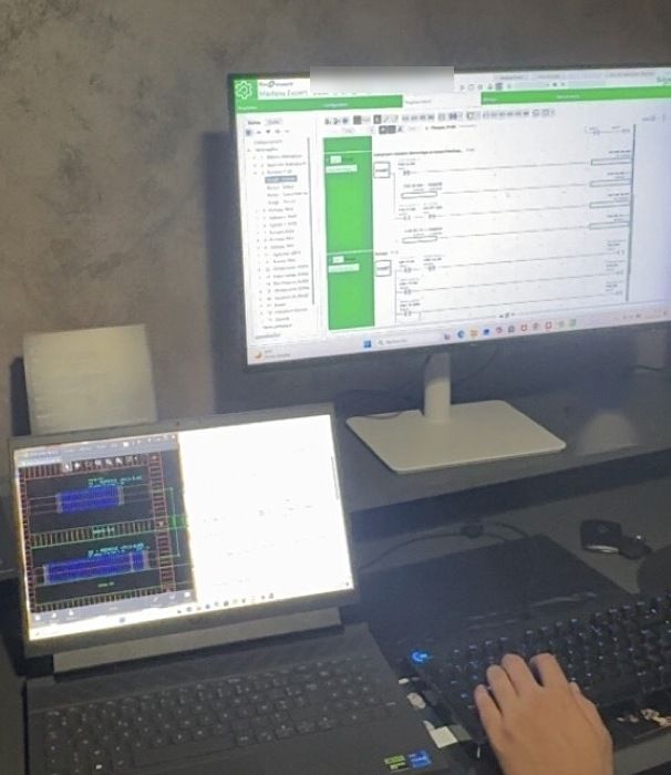 Bureau avec un écran affichant un programme Machine Expert et un ordinateur portable, une main sur le clavier.